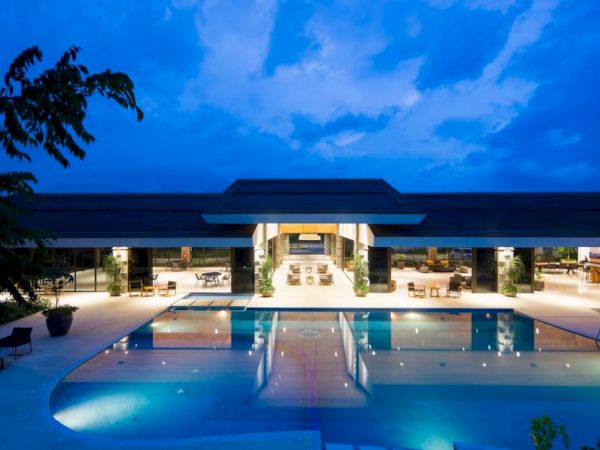 A luxurious modern building with large open spaces and a well-lit swimming pool at dusk, framed by a vibrant evening sky.