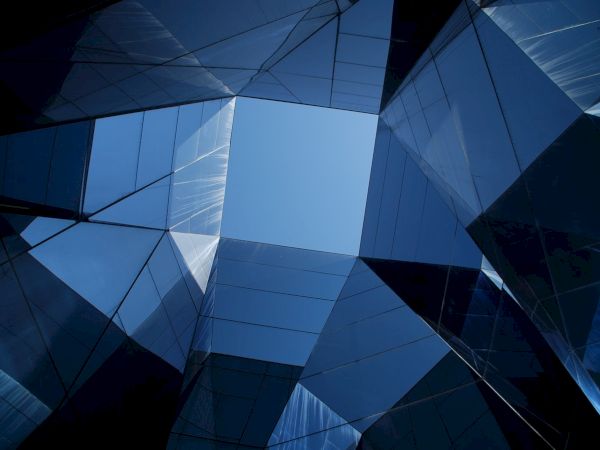 The image shows a geometric architectural structure with reflective glass panels, creating an abstract pattern against a blue sky backdrop.