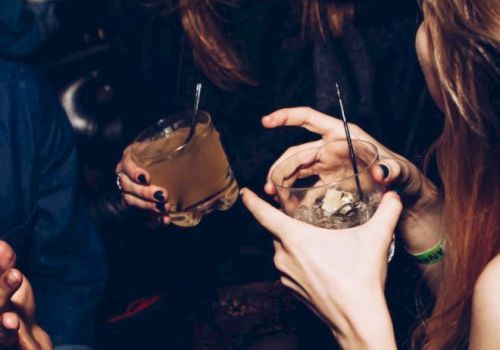 People socializing with drinks in a dimly lit setting, possibly a bar or a party, showing laughter and hand gestures.