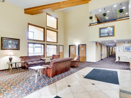 A spacious lobby with leather couches, a lamp on a side table, framed pictures on walls, and hallway leading to rooms.