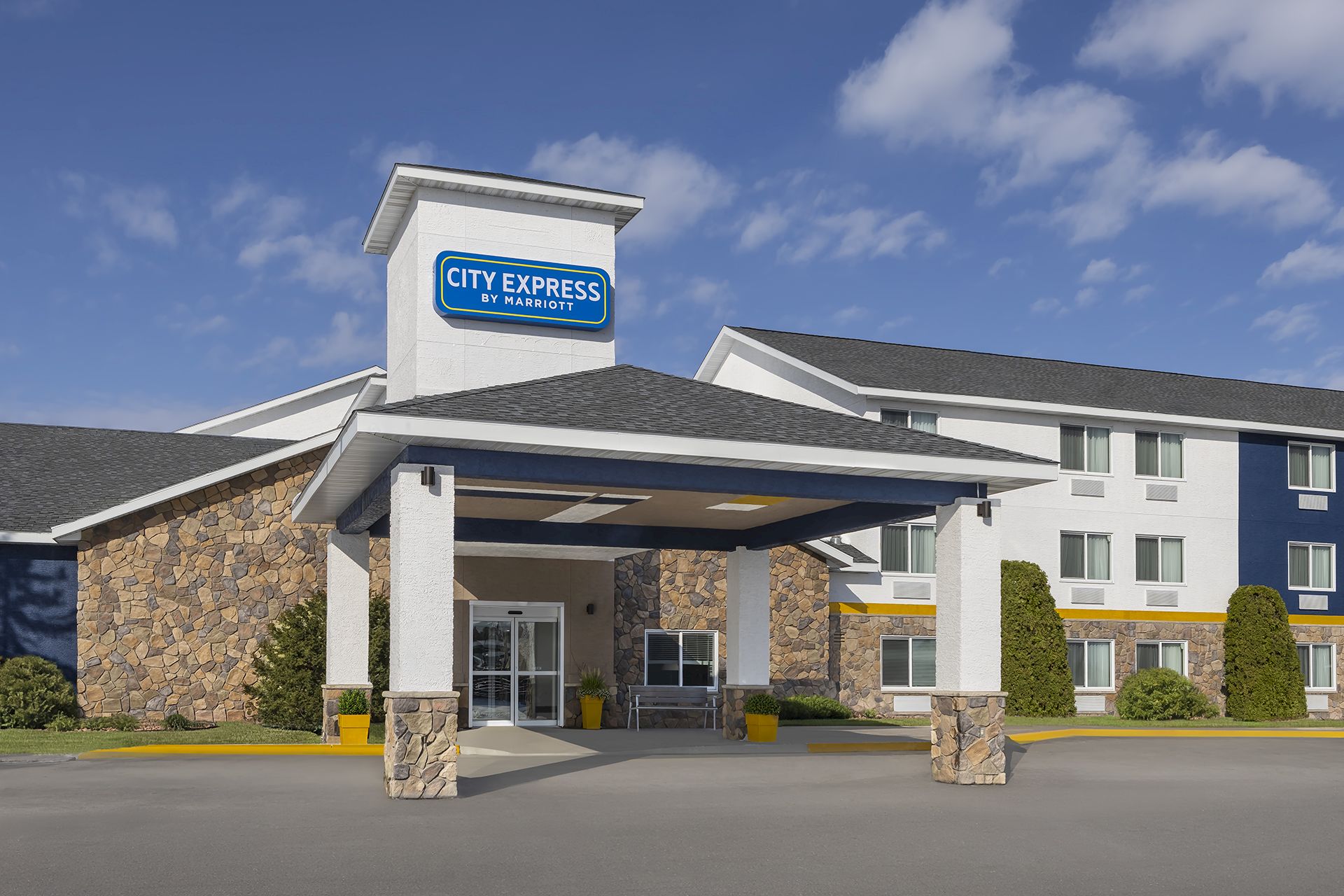 A City Express by Marriott hotel entrance with a &ldquo;CITY EXPRESS&rdquo; sign on a stone-and-white building under a blue sky.