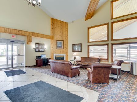 This image shows a cozy room with modern décor, featuring brown leather sofas, a carpet, a computer station, large windows, and wooden accents.