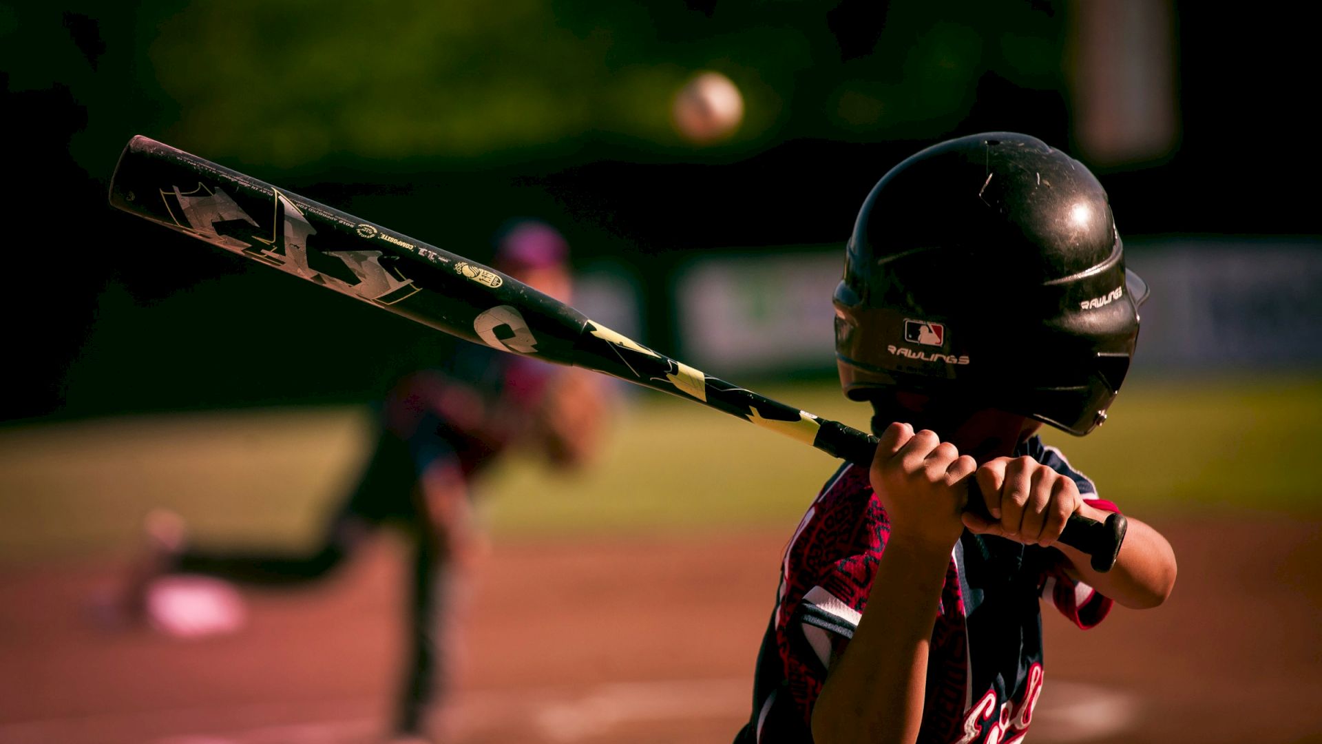 A person prepares to hit a pitched baseball, with a blurred background suggesting motion and focus on the batter.