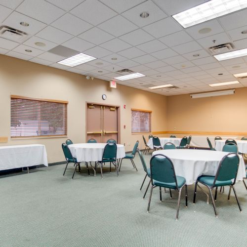 Empty conference room with round tables, chairs, a table against the wall, and a ceiling with fluorescent lights.