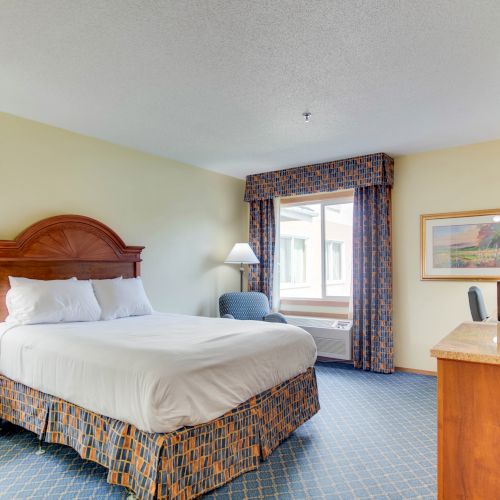 This image shows a hotel room with a queen-size bed, two lamps, a desk, a TV, a microwave, an armchair, and a window with curtains ending the sentence.