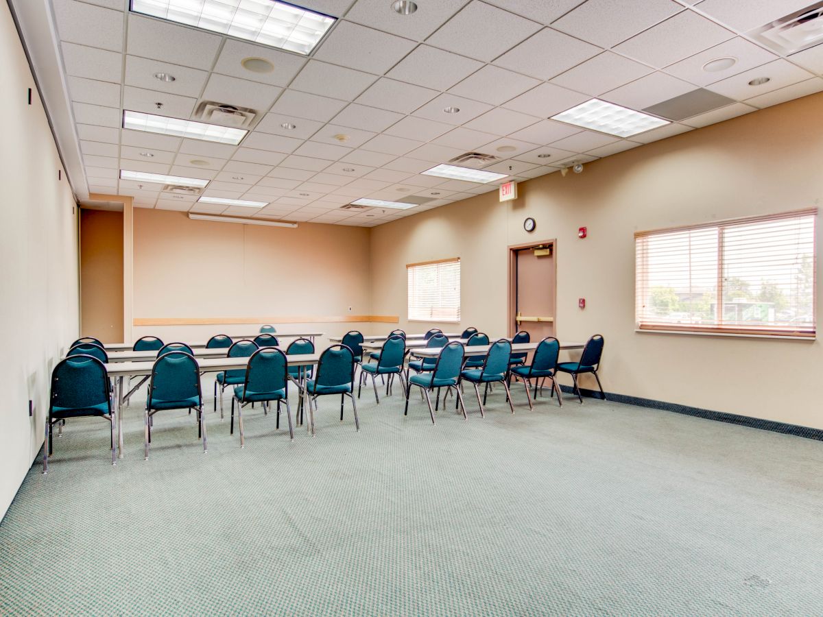 A meeting room with chairs arranged in rows facing a table, well-lit by natural and artificial lighting, clean and empty.