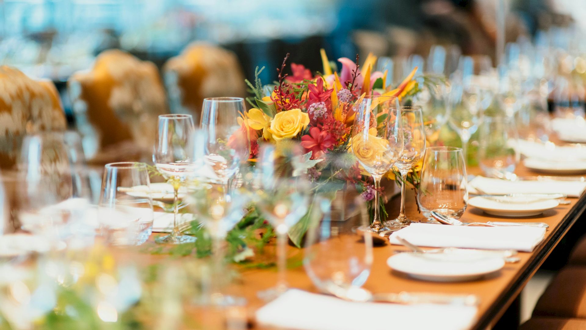 A beautifully set dining table with elegant glassware, white napkins, and a vibrant floral centerpiece, ready for a formal event or gathering.