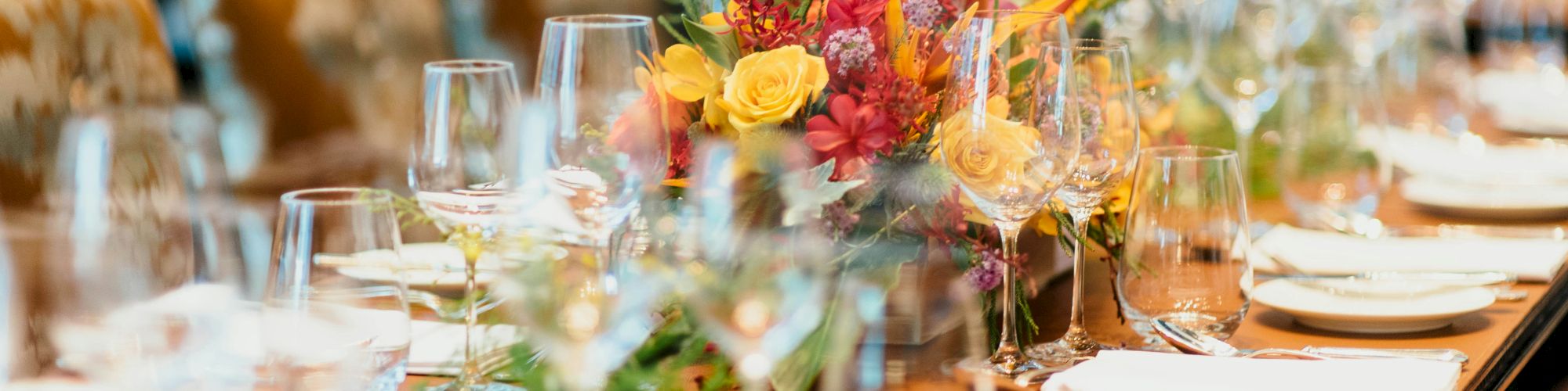 A beautifully set dining table with elegant glassware, white napkins, and a vibrant floral centerpiece, ready for a formal event or gathering.