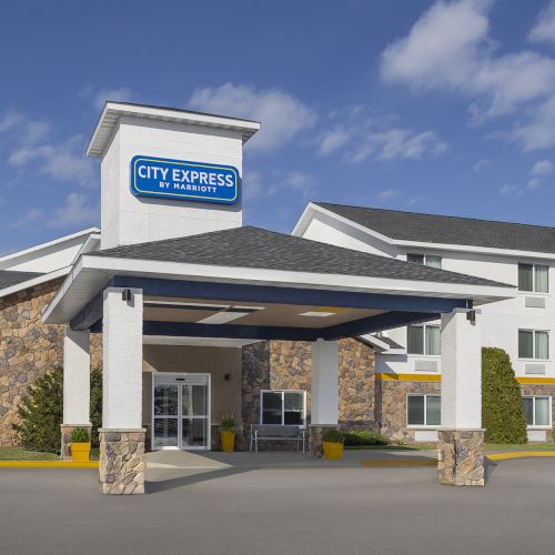 A City Express hotel front with a blue sign, stone columns, a covered drop-off area, and a multi-story blue-and-white building in the background.