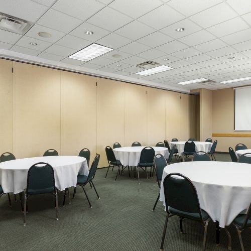 A conference room with round tables covered in white cloths and black chairs arranged for a meeting or event.