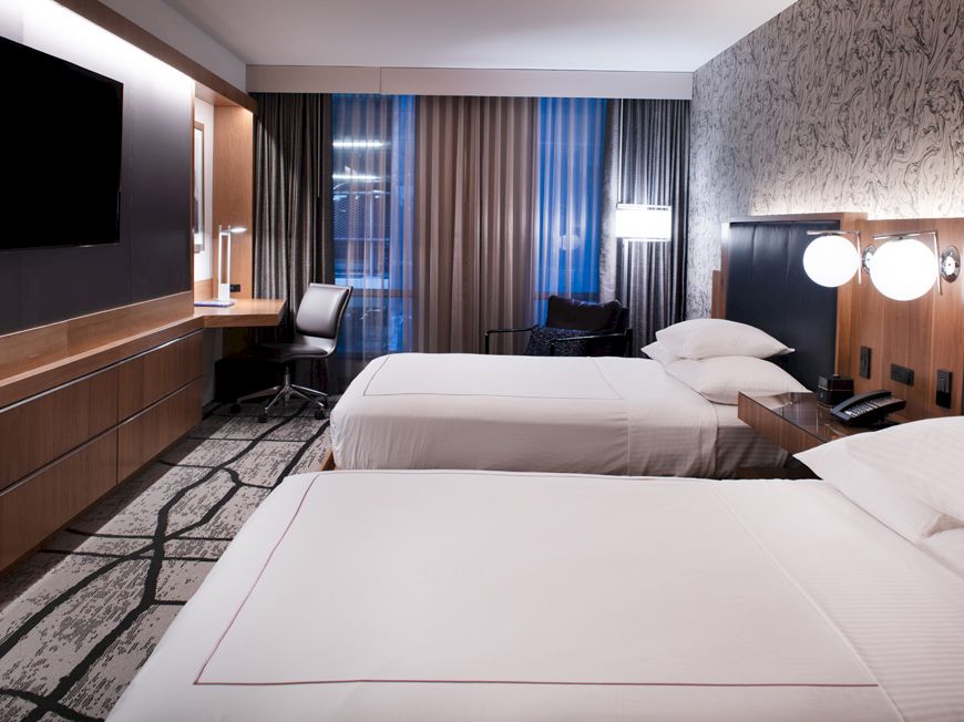 A modern hotel room with two double beds, wall-mounted TV, a workspace with a desk and chair, and stylish decor.